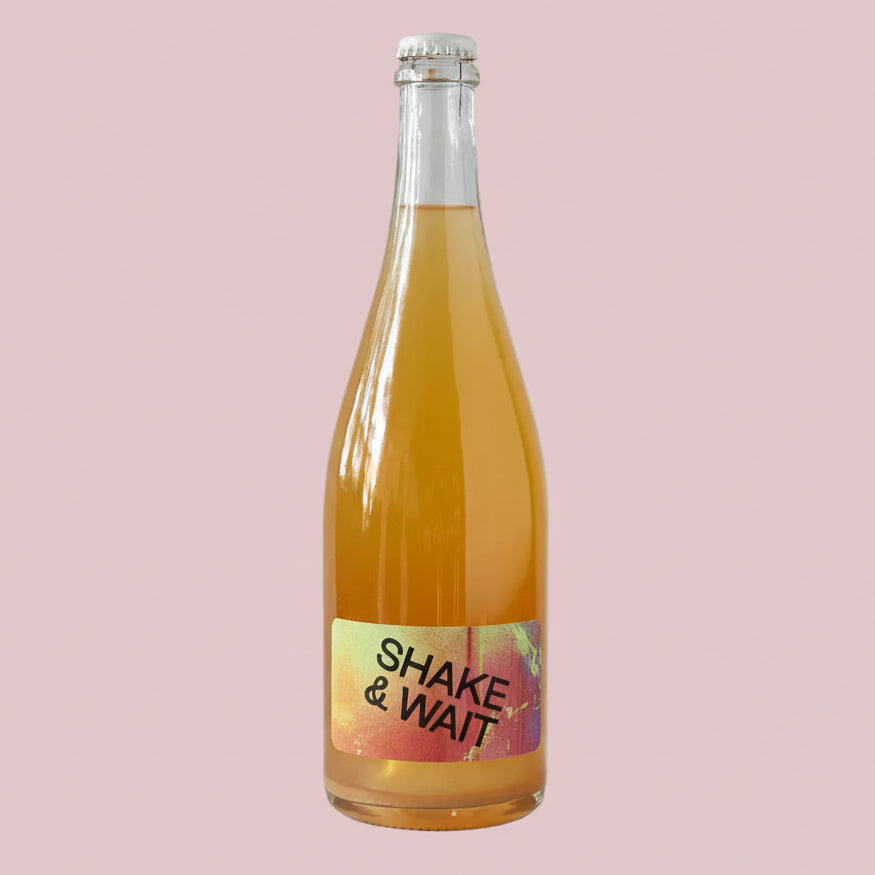 Bottle of orange juice with a 'Shake & Wait' label on a light pink
 background
