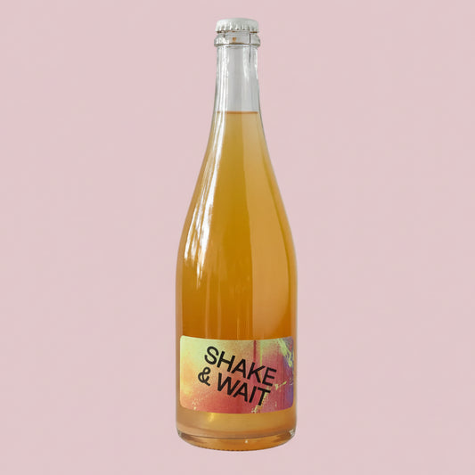 Bottle of orange juice with a 'Shake & Wait' label on a light pink
 background